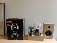 Photo of Bodum Pebo vacuum coffee pot in packaging with burner and original box on table.