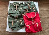 Four vintage Czech canvas backpacks laid out flat on a surface, showing three green and one red backpack with leather buckles and front pockets.