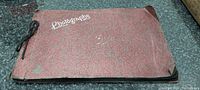 Photo of the antique red textured photograph album showing the cover labeled 'Photographs' tied with a string.