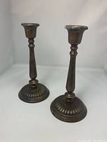 Pair of bronze candleholders shown standing upright, displaying height and shape.