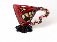 Side view of the red and black high-gloss pottery cup/vase with bee and beehive decorations and pink vine handle.