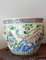 Side view of round ceramic planter featuring colorful Famille Vert style enamel painting of birds, flowers, and aquatic fish with geometric patterned rim.
