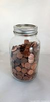 Glass jar filled with a large number of pennies with a metal lid.