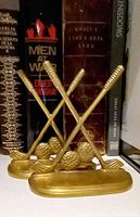 Pair of brass golf club bookends in front of books on shelf, showing crossed clubs with golf balls on oval base