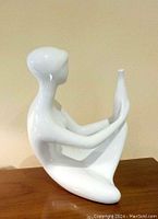 Side view of the white porcelain abstract nude woman statue holding a vase, showing smooth surface and seated pose.