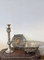 Three silver filigree European items arranged on a table: a fruit bowl, filigree dish, and tall candlestick
