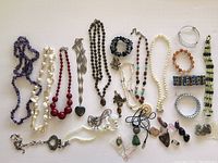 Top-down view of assorted necklaces and bracelets laid out, showing various bead colors, metal pendants and chains, and bracelets of mixed materials.
