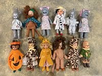 All 12 Madame Alexander dolls shown in a single image arranged on floor, featuring various character costumes and Halloween themes.