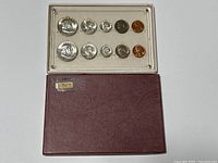 Photo of complete 1957 coin set displayed inside clear plastic holder with corresponding slots, placed on maroon textured folder.