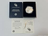 Photo showing the black box with the coin in a protective capsule and the certificate of authenticity unfolded showing printed text and signatures.