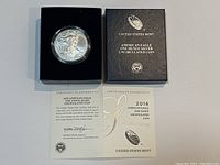 Front view showing coin in protective capsule within black box; certificate unfolded beneath