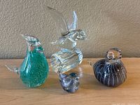 Photo showing all four glass bird figurines together on a flat surface against a neutral wall background.