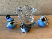 Set of four bird figurines including three blue ceramic birds and one clear glass double bird sculpture on base.