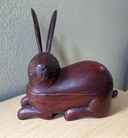 Side view of the carved wooden rabbit box showing the full body, tall ears, and resting paws.