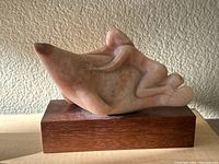 Front angle view of carved stone statue showing human figure riding sea animal on wooden base.