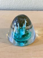 Full view of the clear glass paperweight showing the teal and white staggered center inside.