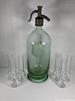 Front view of vintage soda spritzer bottle positioned centrally with six small clear glass tube vases arranged in two groups of three around the base.