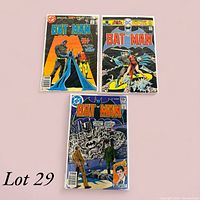 Photo of three Batman comic books showing front covers on a pink background.