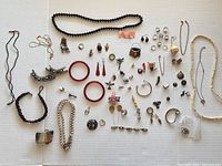 Full overview of assorted jewelry items arranged on white surface including necklaces, rings, earrings, bracelets, bangles, and charms.