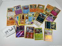 Photo shows 39 assorted Pokemon cards spread on a white background, featuring various characters including Rowlet, Turtonator, and holographic cards.