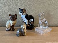 Photo showing all four cat figurines together in seated poses against a beige wall background.
