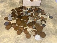 Loose group of approximately 80 mixed metal coins with various sizes and conditions, spread on a surface with a box at the top center.