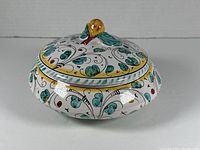 Closed Italian ceramic lidded dish with painted motifs and yellow-green sculpted handle on lid.