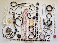 Full view of approx 24 pieces of assorted beaded necklaces and bracelets laid out on white surface