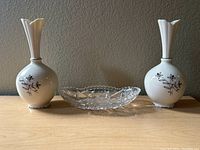 Full lot with two white Lenox bud vases and one clear glass candy dish on wooden surface against a textured wall.