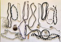 Overview of assorted jewelry pieces laid flat on a white surface showing over a dozen necklaces and pendants with varied beads and chain styles.