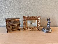 Photo showing three small items: miniature piano, gold-toned framed clock, small woman figurine