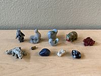 Miniature animal sculptures and small polished stones arranged on a table against a plain background, including alligator, horses, birds, bear, and small stones.
