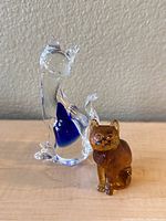 Photo showing both cat figurines: one clear with blue accents and one brown.