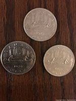 Three 1979 Canadian dollar coins showing canoe and city skyline design on a wooden surface, varying shine and condition.