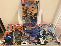 Four Batman comic books displayed upright and flat, showing front covers including Batman: Detective Comics and Batman: The Penguin Affair storylines.