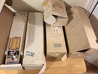Four cardboard storage boxes filled with baseball cards, some boxes open showing tightly packed cards inside, one card visible on each box in front