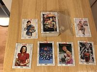 Photo of seven Coca Cola collectible cards arranged on table showing various years and artwork styles.
