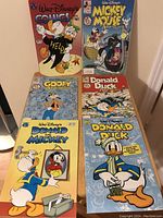 Six Walt Disney comic books standing upright showing cover art featuring Donald Duck, Mickey Mouse, Goofy and titles including Walt Disney's Comics and Stories, Mickey Mouse Adventures, Goofy Adventures, Donald Duck and Donald and Mickey.