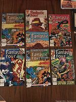 Seven Fantastic Four comic books arranged side by side on a wooden surface, showing cover art and titles.