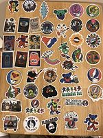 Top view of approximately 46 assorted Grateful Dead stickers on wooden surface showing bears, skulls, rainbows, band-related images