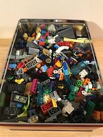 Top view of a metal tin filled with assorted LEGO pieces in multiple colors and shapes.