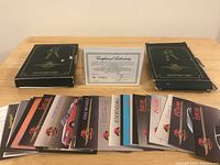 Two black collector card boxes with gold detailing on top, one open showing spread out collector cards featuring car brands and logos. Centered Certificate of Authenticity is visible between the boxes.