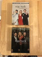 Two Nip/Tuck DVD box sets, Seasons 2 and 3, stacked on wooden surface.