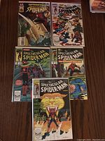 Six Spiderman comics displayed on a wooden surface, visible titles include Sandman Untold Tales of Spiderman and The Spectacular Spiderman series. Comics are in protective bags with backing boards.