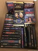 Photo showing a variety of Star Trek paperback books in a box, some with visible wear and a few other sci-fi paperback novels.