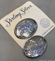 Two oval sterling silver brooches on original card, marked Canadian Jewellers, Made in Canada, with etched floral design.