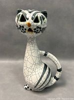 Front and side view photo of white and black crackled ceramic sitting cat sculpture with cut-out eyes and mouth by Livia Gorka.