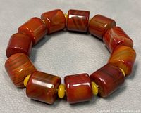 Close-up of the reddish-brown cylindrical onyx beads and yellow spacer beads arranged on a stretch cord.