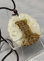 Close-up of Chinese jade pendant showing dual-tone white and brown jade with intricate traditional carving and attached cord chain with red bead.