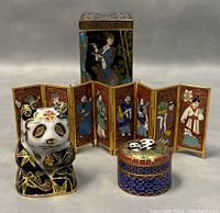 Front angle photo showing the cloisonné panda figurine, the miniature seven-panel folding screen with painted human figures, and the small round cloisonné box with panda lid, all arranged in front of the antique cloisonné brass box.